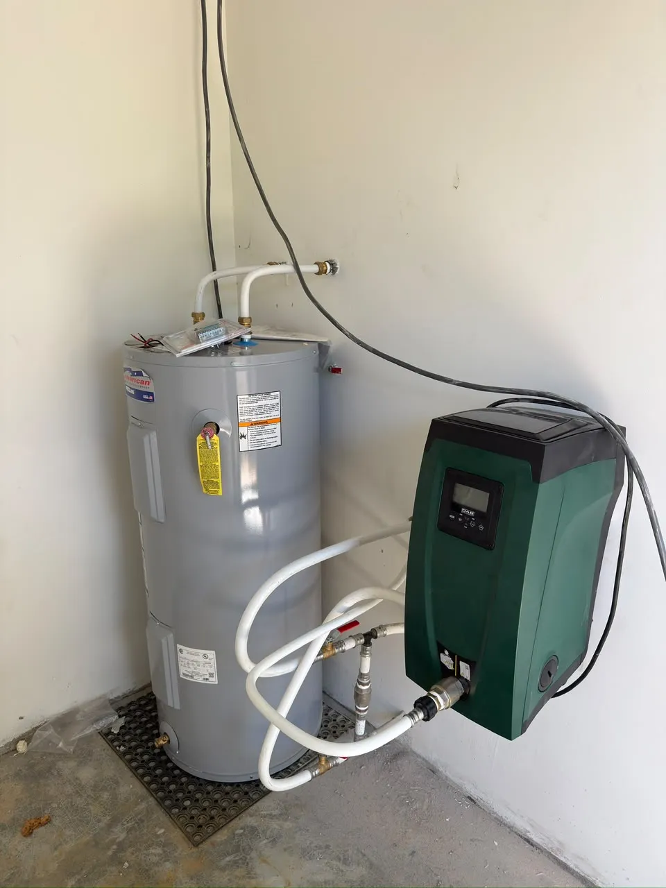Elektrische boiler naast een drukpomp met display aan de wand, aangesloten met witte waterleidingen