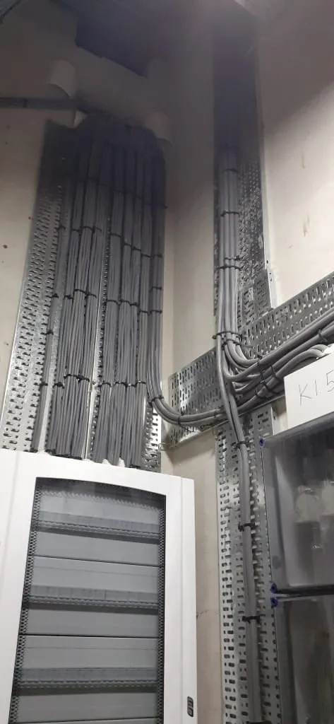 Bundels grijze kabels netjes vastgebonden in kabelgoten boven een groepenkast